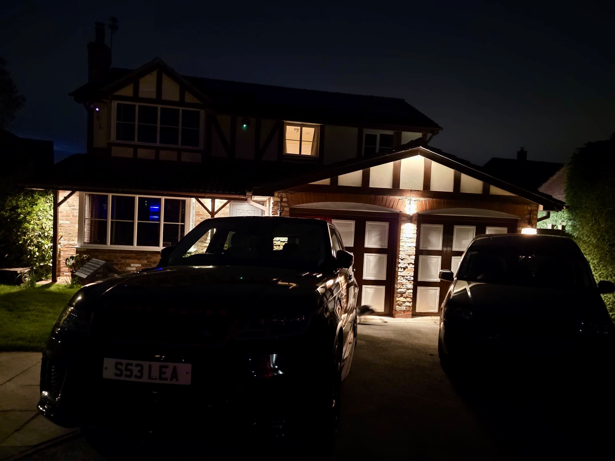 Tudor-style home with lit porch and driveway at night