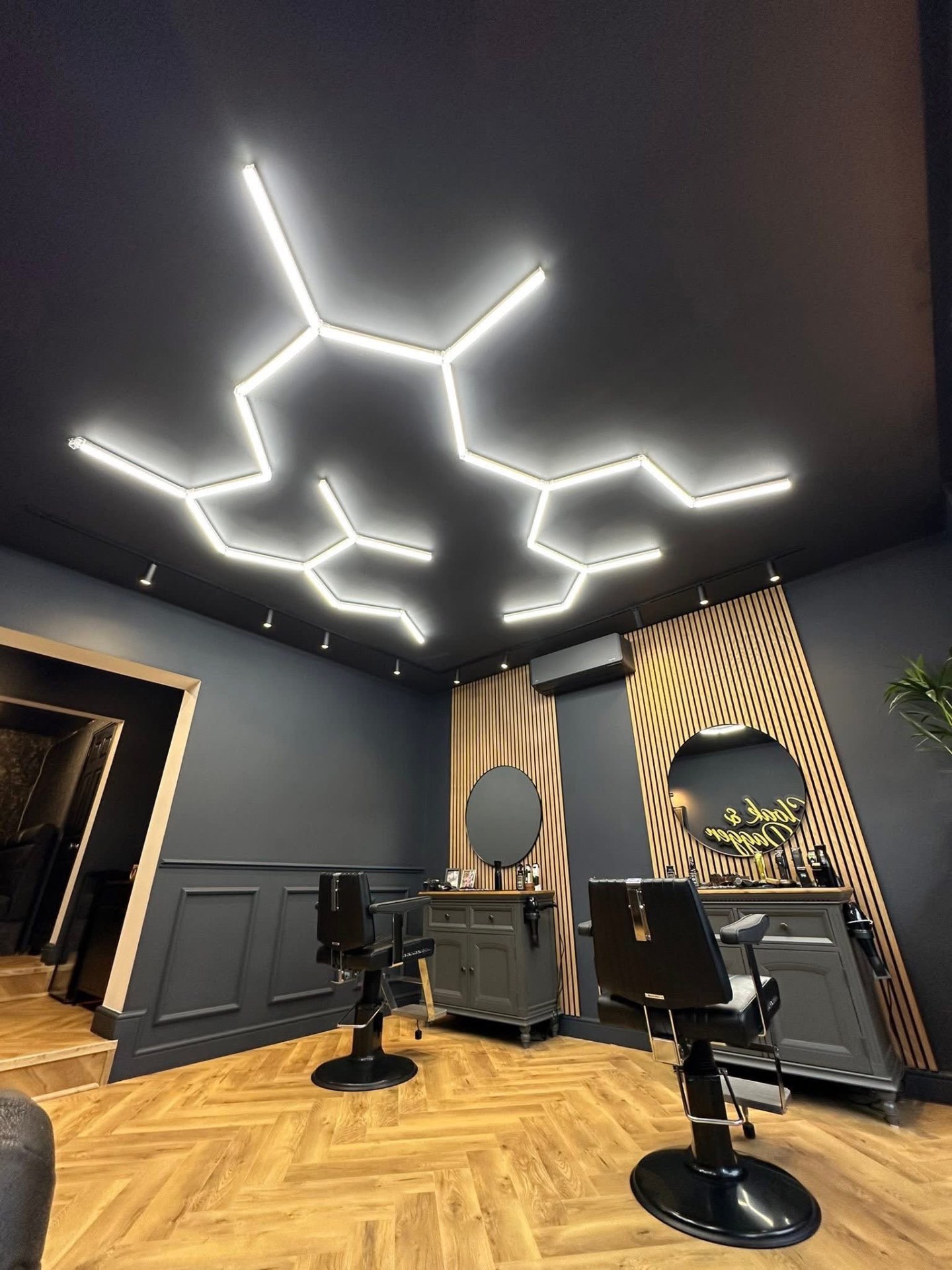 Ceiling-mounted hexagonal LED lighting rig above barber chairs